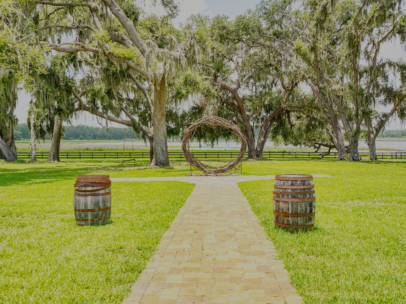 Brick pathway leading to circular wooden structure beneath large oak trees at Covington Farm event grounds.